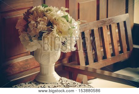 flower vase with decoration items placed on old wooden table and antique chair with vintage filter. soft focus