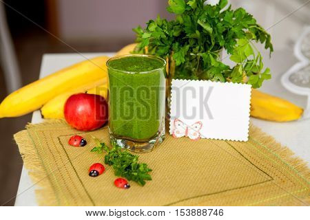 Vitamin smoothie in glass linen napkin on the kitchen table. On the table as banana, apple and parsley and place for text