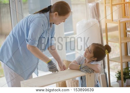 Asian lovely girl helping her mother assembling new DIY furniture at home together