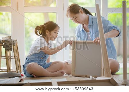 Asian lovely girl helping her mother assembling new DIY furniture at home together