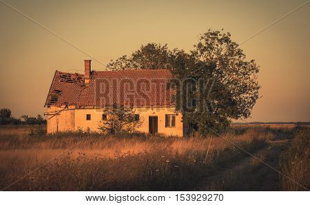 Vintage photo of abandoned old house in sunset