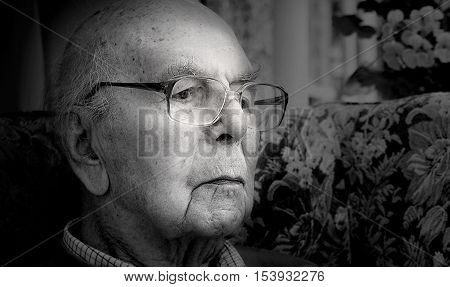 Portrait of 95 years old English man sitting in chair in domestic environment. Black and white