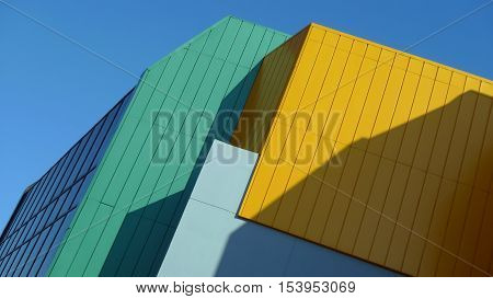 Building fragment cladding colored stripes of yellow, turquoise, blue. Against the background of the blue sky.