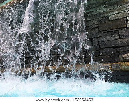 Fresh Water splashing and falling motion image cascading into pool from waterfall over natural stone wall