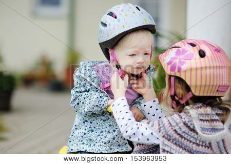 Little Girl Hepling Her Sister To Put A Helmet