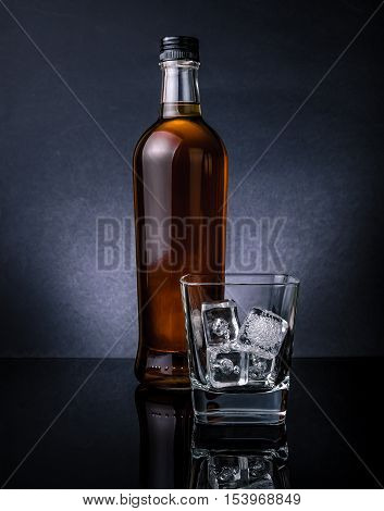 Whiskey With Ice Cubes In Glass Near Bottle On Black Background, Cold Atmosphere