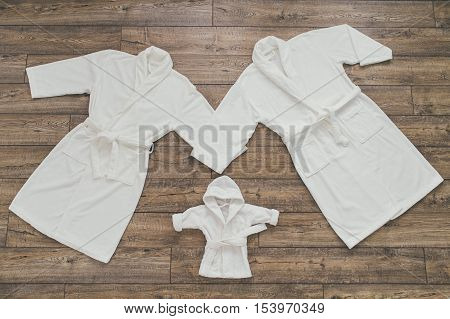 Three white Bathrobe for family on wooden background