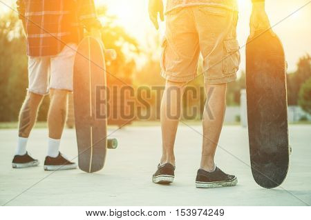 Skaters friends outdoor in urban city with skateboards in their hands - Young people training longboard extreme sport - Friendship concept - Warm filter