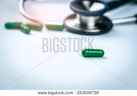 Selective Focus On Green Capsule Pills On Blurred Stethoscope And Green Capsule Medicine Background.