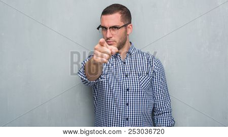 Young caucasian business man over grey grunge wall pointing with finger to the camera and to you, hand sign, positive and confident gesture from the front