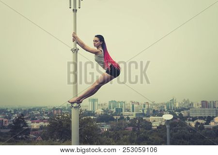 Girl Athlete Dancing On A Pole. Paul Dance On The Background Of The City. Striptease On The Lantern 