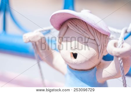 Cute Pink Ceramic Girl Doll Is Playing Rope Swing On The Blue Metal House Fence, She Seems Enjoying 