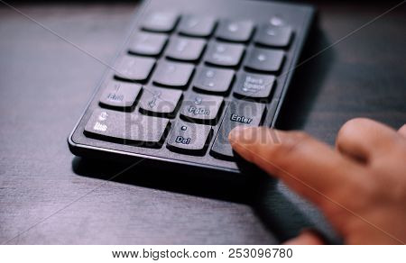 An Index Finger Is Pressing On Enter Button Of A Black Plastic Numeral Keypad In Order To Make Decis