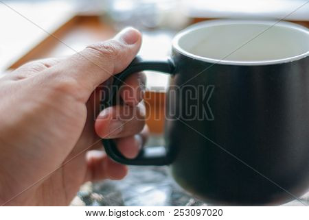 A Left Tan Skinned Hand Is Holding A Black Coffee Mug Going To Lift It Up To Drink In Order To Repel