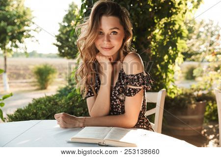 Image of cute beautiful young woman sitting in cafe outdors in park with book.