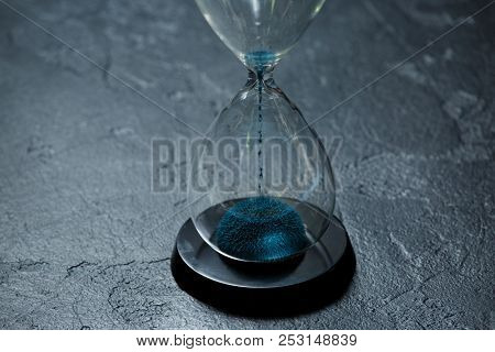 Photo of glass hourglass with blue sand on black stone background
