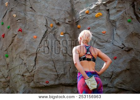 Photo from back of sporty woman climber with bag of soap against rock boulder