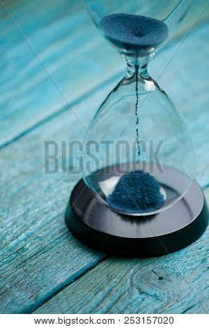 Photo of hourglass with blue sand on wooden background,