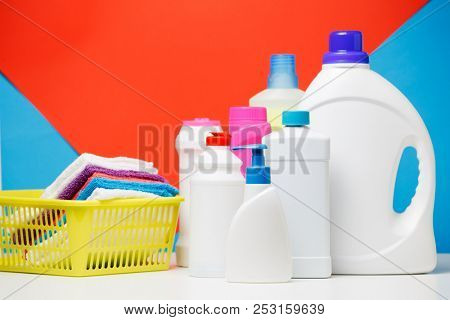 Photo of different bottles of cleaning products and colored towels in basket isolated on red, blue background