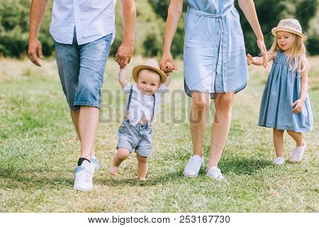 Parents Holding Hands With Children And Walking On Green Feild Together