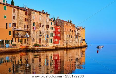 Rovinj, Istria, Croatia. Antique medieval houses at coastline of Adriatic sea. Sunrise with blue sky and fishing boat on horizon. Calm and silent summer morning.