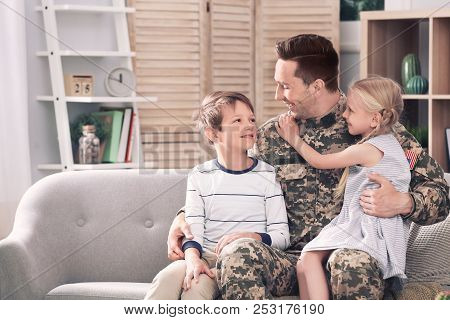 Young Man In Military Uniform With His Children On Sofa At Home