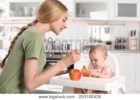 Woman Feeding Her Child In Highchair Indoors. Healthy Baby Food