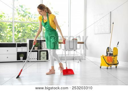 Young Woman With Broom And Dustpan Cleaning In Office