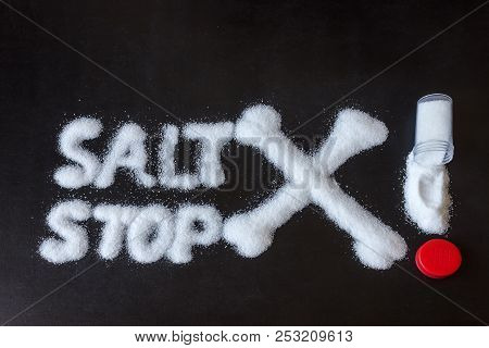 Salt Scattered On Black Surface. Drawn Word- Salt, Stop And Crossed Bones. Concept- Healthy Food, Di