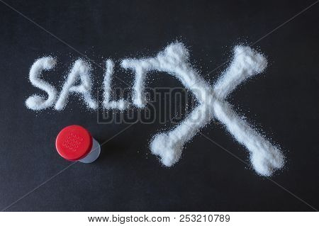 Salt Scattered On Black Surface. Drawn Word- Salt And Crossed Bones. Concept- Healthy Food, Diet, Ha