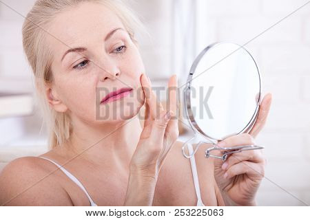 Forty Years Old Woman Looking At Wrinkles In Mirror. Plastic Surgery And Collagen Injections. Makeup
