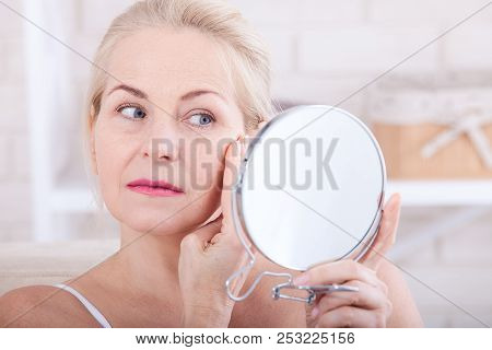 Forty Years Old Woman Looking At Wrinkles In Mirror. Plastic Surgery And Collagen Injections. Makeup