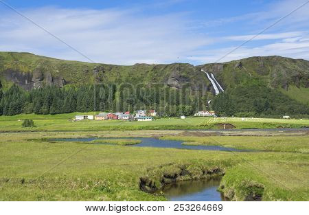 Rural Landscape With Colorful Farm Houses, Blue River Stream On Green Grass Meadow With Spruce Tree 