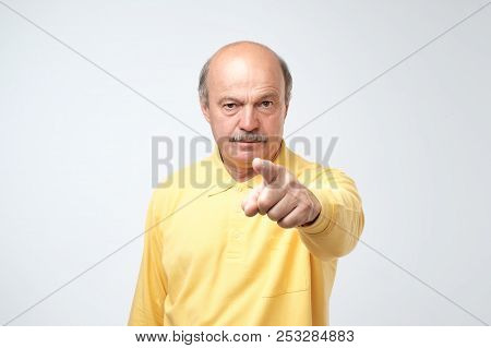 Portrait Of Serious Senior Man With Warning Finger And Yellow T-shirt Shirt Against Light Gray Backg