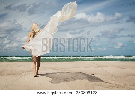 Bare Blond Woman With White Veil Walking On Sunny Sea Beach