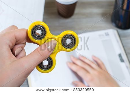 Close Up Photo Of Fidget Spinner In Hand. Student Playing Yellow Fidget Spinner While Studying