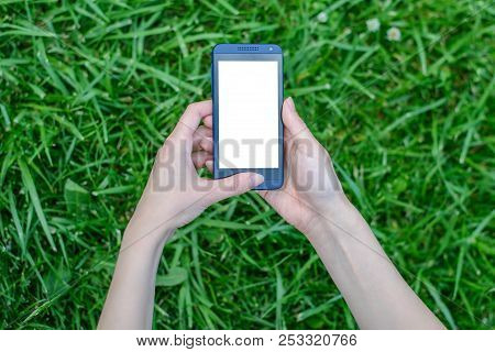 Woman Holding Smartphone With White Empty Touchscreen In Hands Over Background Of Grass