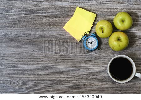 An Image Of Apples, Cup Of Coffee, Alarm Clock, Stickers Lying On A Wooden Table