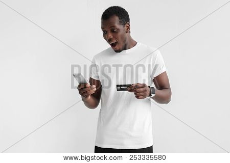 Indoor Portrait Of Young Handsome African Man Standing Isolated On Grey Background Holding Smartphon