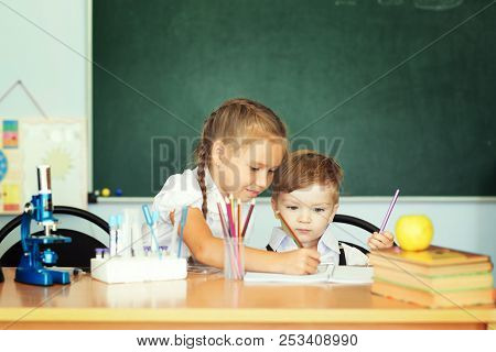 Cute Little Girl Helping Her Younger Brother At Classroom In School Or Pre-school