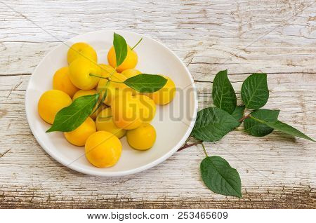 Yellow Cherry Plums On A White Saucer And Small Twig Of Cherry-plum Tree On An Old Rustic Wooden Sur