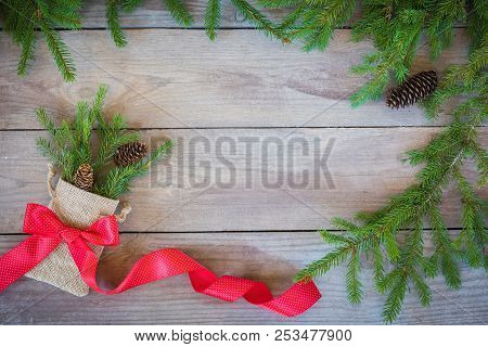 Christmas Firbranch With Cones, Red Polka Dot Ribbon In The Rustic Bag On Old Wooden Background