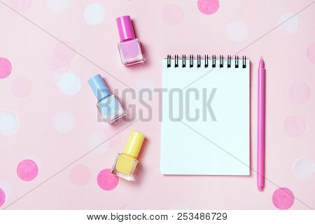 Empty Note Pad And Colorful Nail Polishes On Pink Confetti Background.