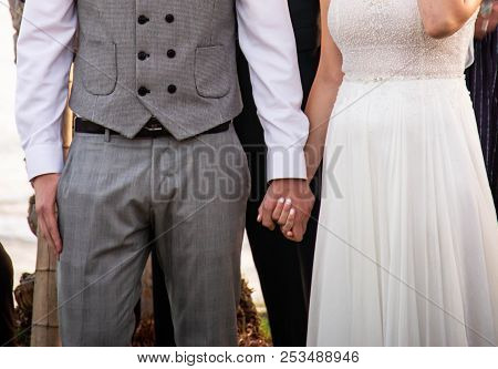 Happy Bride In White With Stones Dress And Bridegroom In Gray Fashionable Suit Holding Hands