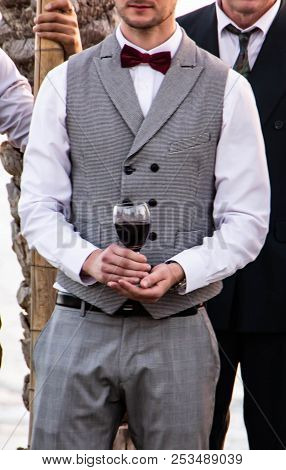 A Happy Groom In A Gray Fashion Suit Is Holding A Glass Of Red Wine