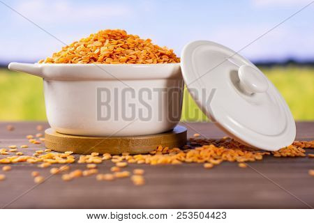 Lot Of Whole Raw Red Lentils In A Ceramic Stewpan With Green Wheat Field In Background