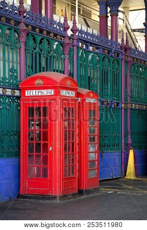 Two red booths in two different sizes with green and blue iron fence in background in Smithfield market in London UK