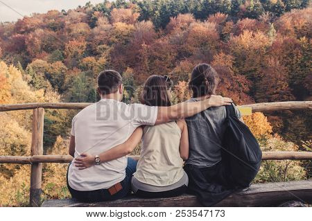 Three People Hugged Each Other Sitting On Wooden Benches And Watch The Beautiful Autumn Landscape, C