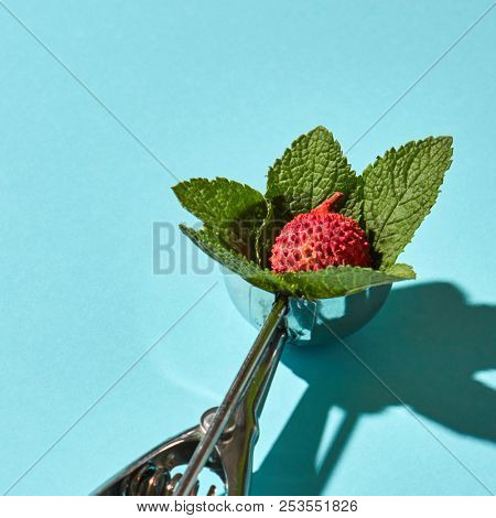 Creative composition from litchi fruit with mint leaves in the metal spoon for ice cream on a blue glass background with shadows. Food modern style.