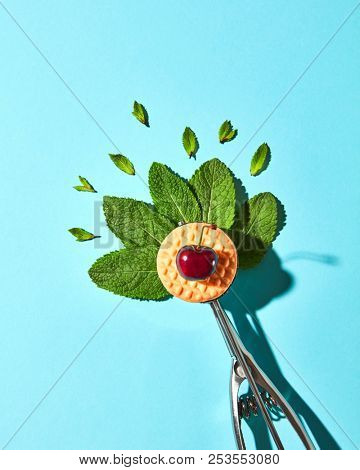 Creative composition from mint leaves in the metal spoon for ice cream and biscuit with cherry on a blue glass background with shadows. Food modern style, top view.